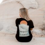 female leaning against a rock with a White Sands National Park shirt and blue jeans