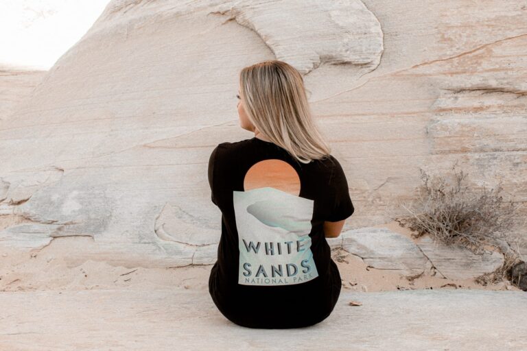 female leaning against a rock with a White Sands National Park shirt and blue jeans
