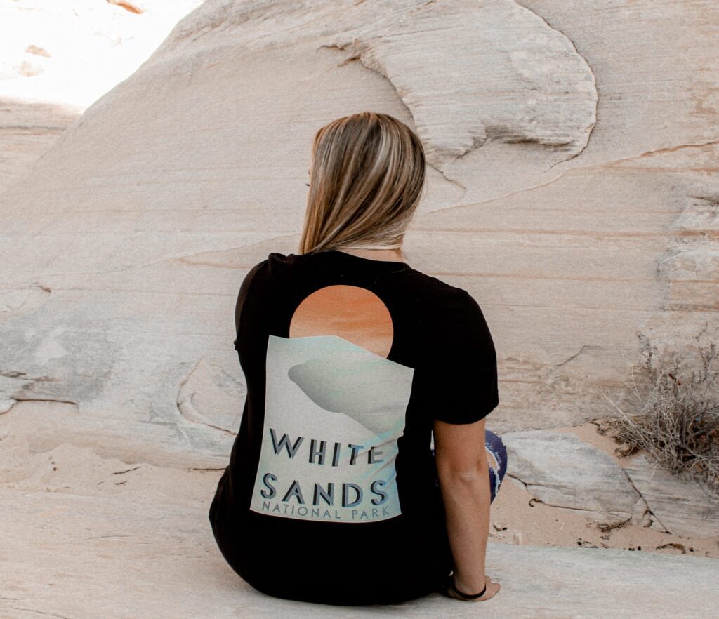 Female sitting against a rock with a white sands national park t-shirt
