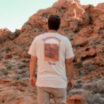 male gazing over a valley of red rocks wearing a cream colored canyonlands t-shirt