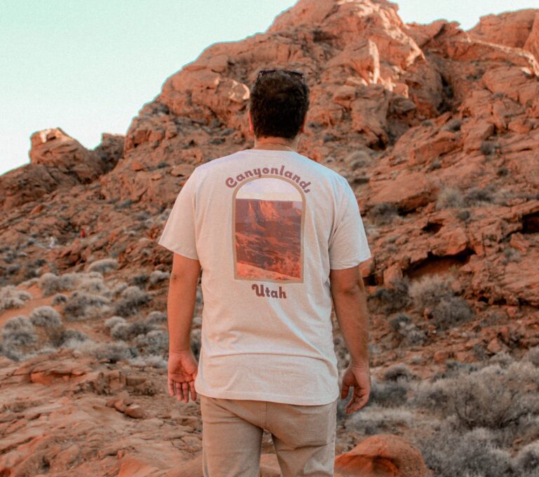 male gazing over a valley of red rocks wearing a cream colored canyonlands t-shirt