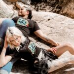 two females laying next to eachother in the mountains with a black yellowstone national park shirt