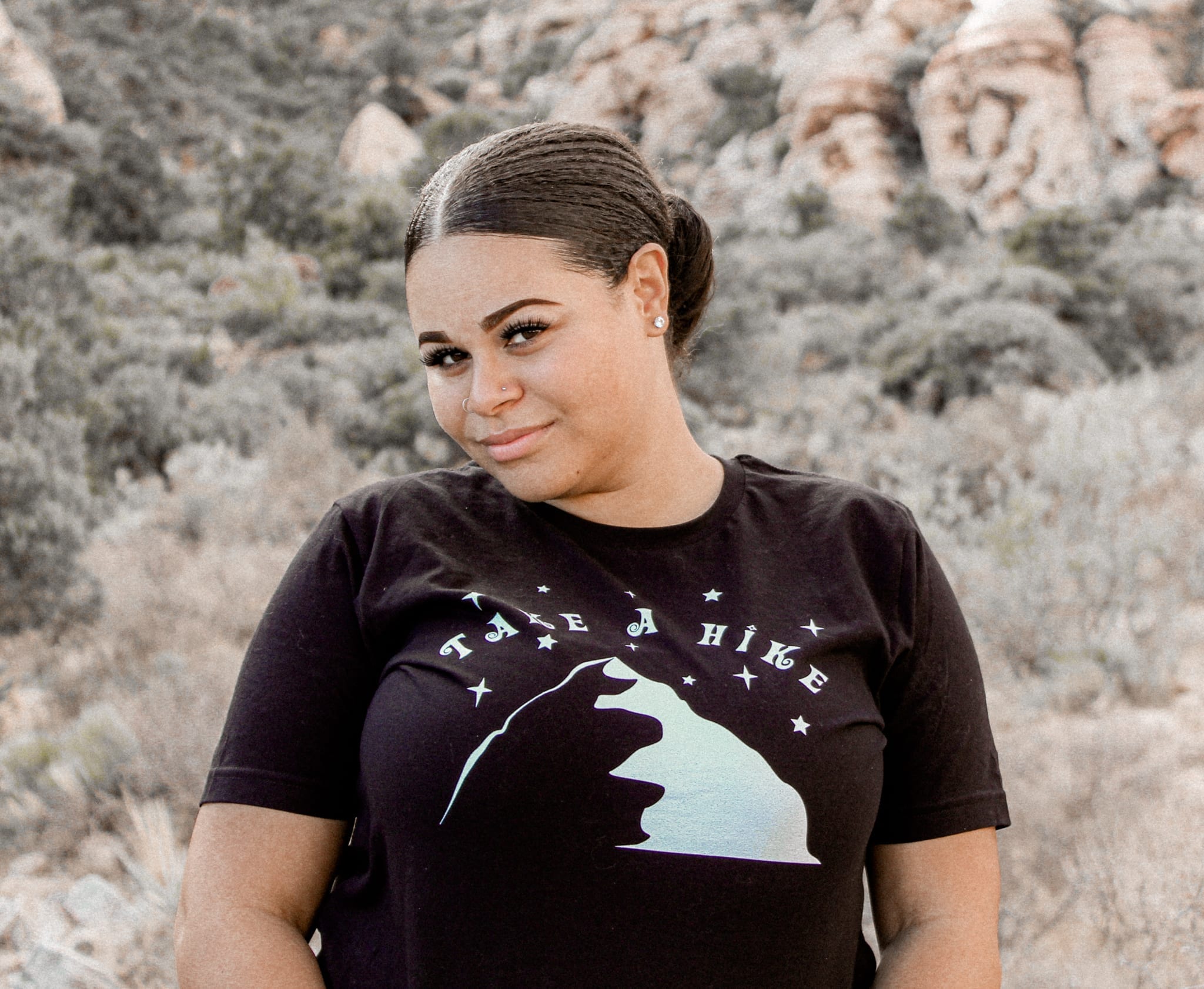 female with a black take a hike shirt with green hills behind her