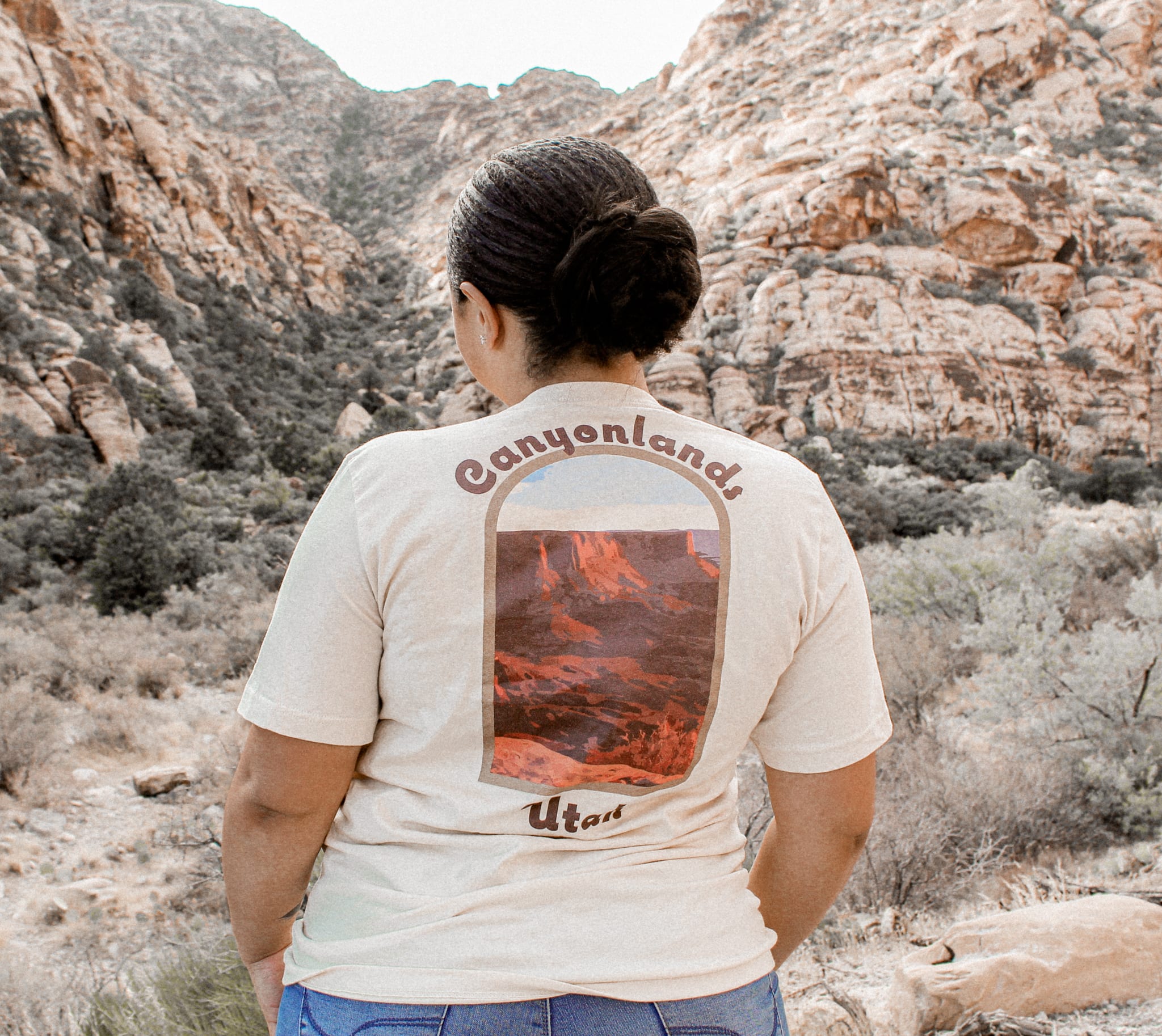 woman standing in a green valley in a cream colored canyonlands t-shirt