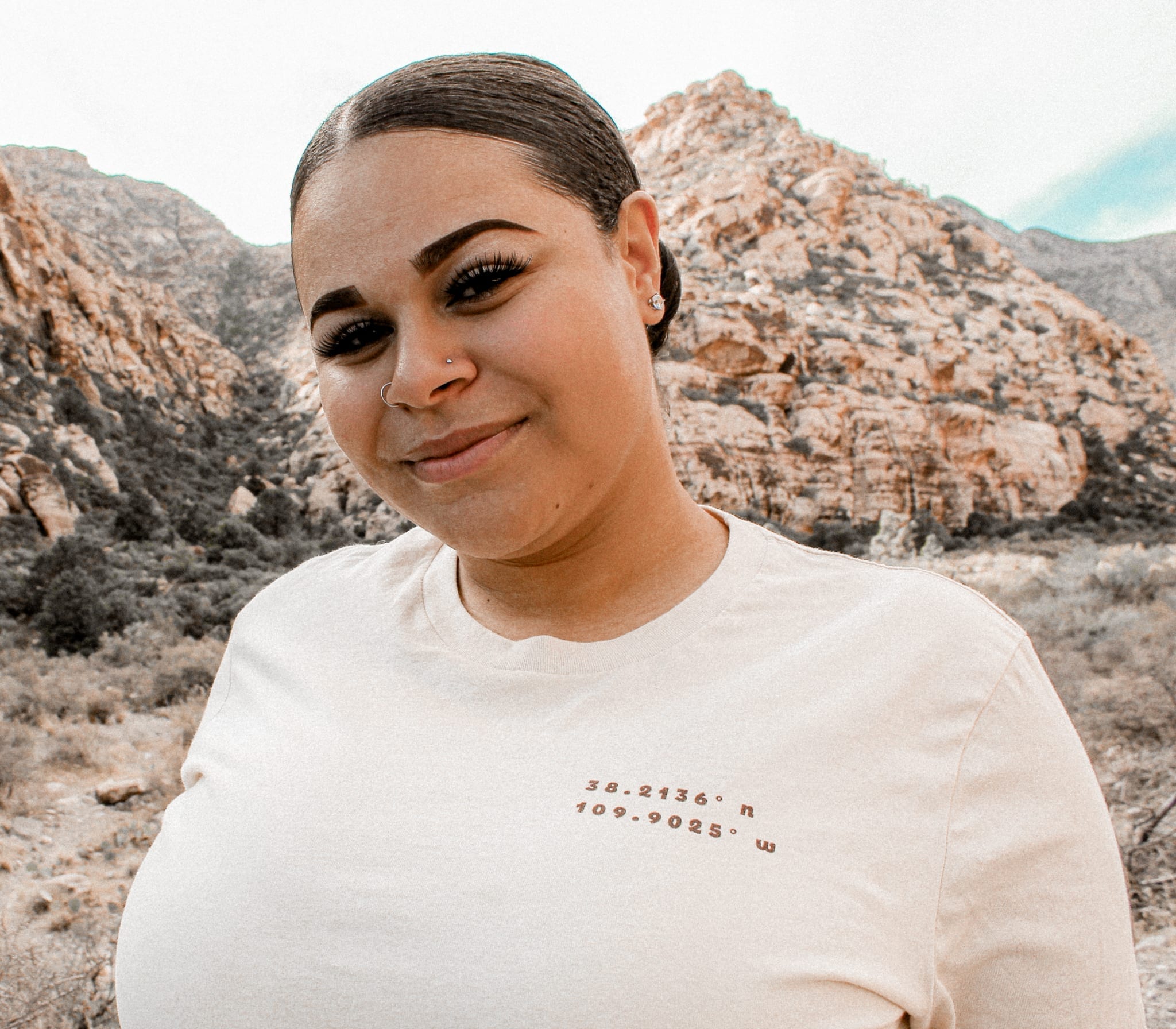 woman wearing a t-shirt with canyonlands coordinates with green hills behind her