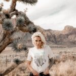 woman standing next to a joshua tree in a cream colored saguaro national park t-shirt